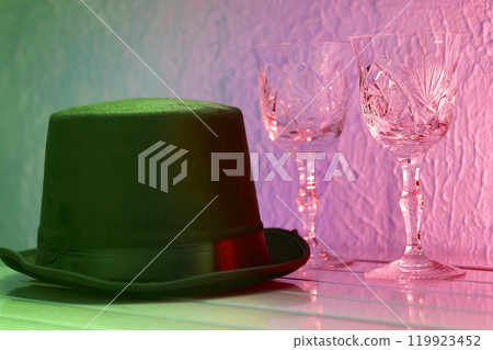Black hat, shining crystal wine glasses on pink light Black hat, shining crystal wine glasses on pink light 119923452