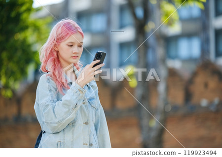 A woman with pink hair is looking at her cell phone A woman with pink hair is looking at her cell phone 119923494
