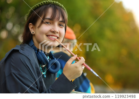 Creative Spirit. The Young Artist in Nature. a young female artist passionately painting outdoors, with brushes and paints in her hands. Surrounded by the beauty of nature, she is fully immersed in 119923498
