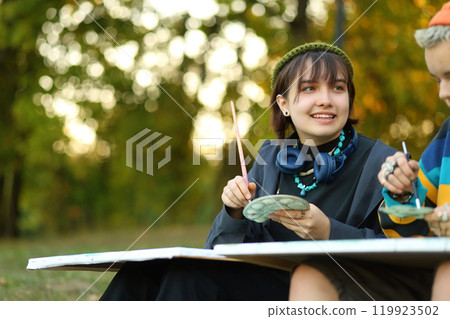 Creative Spirit. The Young Artist in Nature. a young female artist passionately painting outdoors, with brushes and paints in her hands. Surrounded by the beauty of nature, she is fully immersed in 119923502