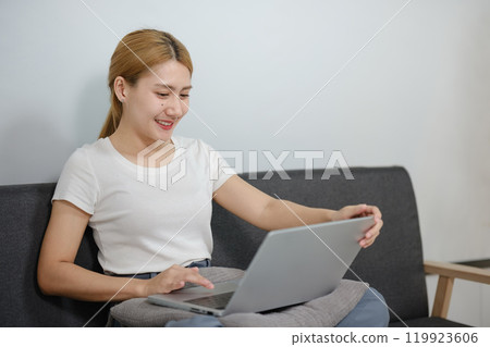 A woman is sitting on a couch and using a laptop A woman is sitting on a couch and using a laptop 119923606
