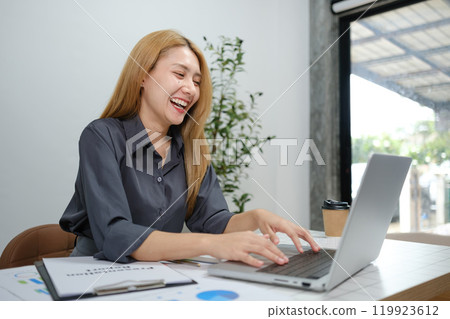 A woman is sitting at a desk with a laptop and a cup of coffee A woman is sitting at a desk with a laptop and a cup of coffee 119923612