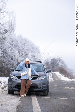 Woman in Winter Clothing by SUV on Snowy Road Woman in Winter Clothing by SUV on Snowy Road 119923613