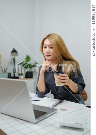 A woman is sitting at a desk with a laptop and a cup of coffee A woman is sitting at a desk with a laptop and a cup of coffee 119923614