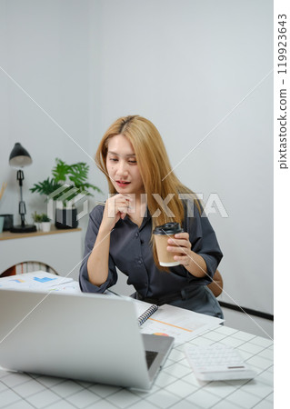 A woman is sitting at a desk with a laptop and a cup of coffee 119923643