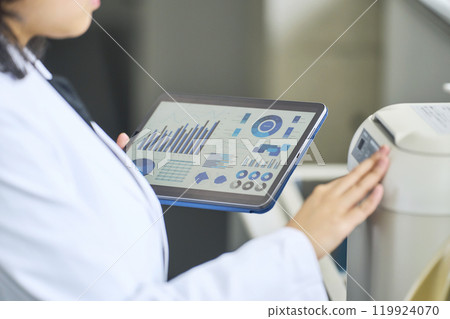 A researcher using experimental equipment while looking at a tablet screen 119924070