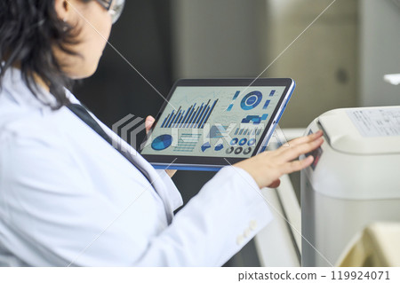 A researcher using experimental equipment while looking at a tablet screen A researcher using experimental equipment while looking at a tablet screen 119924071
