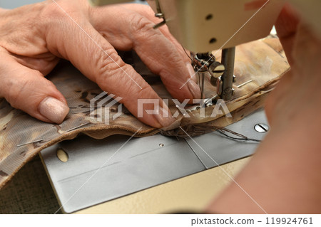 The hand of a seamstress that holds the fabric in a sewing machine. 119924761