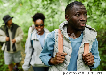 Multiethnic group of tourists exploring forest together with focus on adult African American man looking away in foreground copy space Multiethnic group of tourists exploring forest together with focus on adult African American man looking away in foreground copy space 119924998