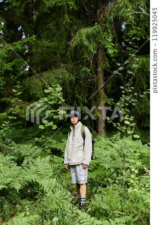 Vertical wide angle shot of young man as solo tourist standing in vibrant forest scenery and wearing backpack copy space Vertical wide angle shot of young man as solo tourist standing in vibrant forest scenery and wearing backpack copy space 119925045