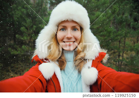 Happy smiling woman taking selfie with smartphone in winter park against Christmas tree, using phone Happy smiling woman taking selfie with smartphone in winter park against Christmas tree, using phone 119925150