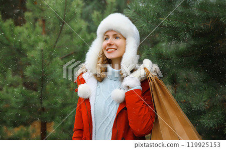 Happy smiling young woman with shopping bag in winter against Christmas tree, holiday shopping Happy smiling young woman with shopping bag in winter against Christmas tree, holiday shopping 119925153