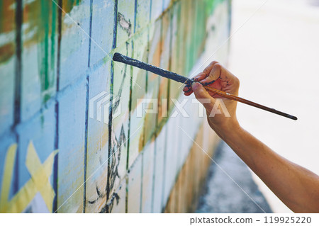 Female artist's hand with a brush painting graffiti on the wall  119925220