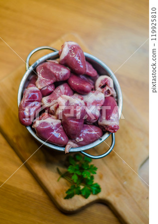 Raw duck hearts with parsley in metal pot on wooden chopping board . High quality photo 119925810