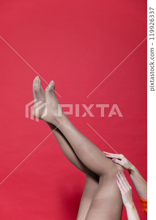 Beautiful slender female legs in tights, stockings on a red background Beautiful slender female legs in tights, stockings on a red background 119926337