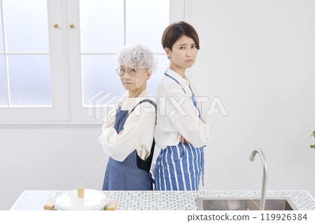 Mother-in-law and daughter-in-law who don't get along well, kitchen, looking at camera Mother-in-law and daughter-in-law who don't get along well, kitchen, looking at camera 119926384