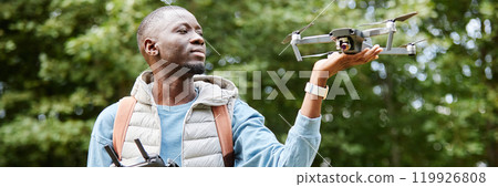 Header image of smiling African American man holding drone while enjoying nature videography in green forest copy space Header image of smiling African American man holding drone while enjoying nature videography in green forest copy space 119926808