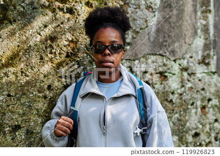 Waist up portrait of Black young woman travelling solo in nature and looking at camera wearing sunglasses 119926823