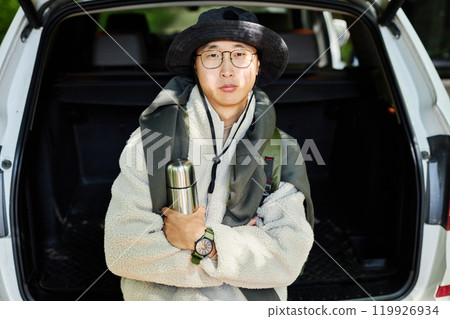 Waist up portrait of adult Asian man wearing hiking gear and eyeglasses looking at camera standing by car at nature trail copy space Waist up portrait of adult Asian man wearing hiking gear and eyeglasses looking at camera standing by car at nature trail copy space 119926934