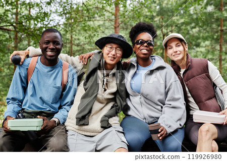 Front view portrait of diverse group of tourists posing together and smiling at camera while taking break on nature trail Front view portrait of diverse group of tourists posing together and smiling at camera while taking break on nature trail 119926980