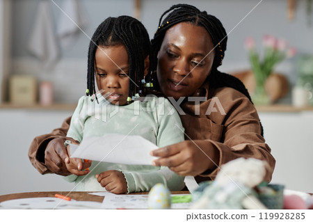 Mother and young daughter engaging in creative artwork together Mother showing daughter how to draw while spending quality time in cozy home environment Mother and young daughter engaging in creative artwork together Mother showing daughter how to draw while spending quality time in cozy home environment 119928285