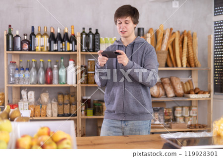Young male seller with phone in grocery store 119928301