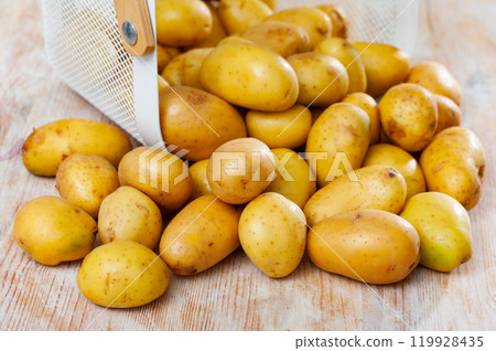 Raw potatoes in white wire basket on wooden background 119928435