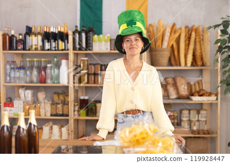 Positive female store clerk in green hat is preparing to meet customers on eve of St. Patricks Day 119928447
