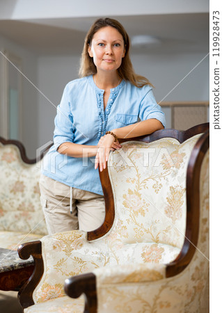 Calm female standing and leaning on the chair in the living room at home Calm female standing and leaning on the chair in the living room at home 119928473