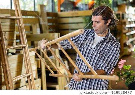 European gardener is attentively examining a bamboo ladder 119928477