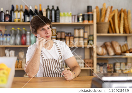 Portrait of confident young salesperson sitting at counter in supermarket Portrait of confident young salesperson sitting at counter in supermarket 119928489