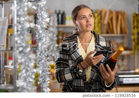 Young woman in store chooses bottle of sparkle wine, scan QR code on label 119928516