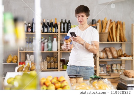 Young man in store chooses canned beans, scan product label with phone. 119928522