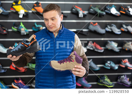 Attentive male athlete chooses sports winter shoes for hiking in sports store 119928550