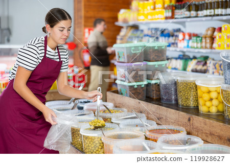 Young girl in supermarket, scooping marinated olives from bucket with ladle 119928627