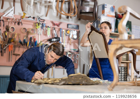 collected male restorer carefully covers carved wooden frame of antique mirror with layer of varnish 119928656