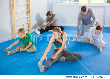 Family in gym during group sports training under guidance of trainer performs stretching on floor Family in gym during group sports training under guidance of trainer performs stretching on floor 119928720