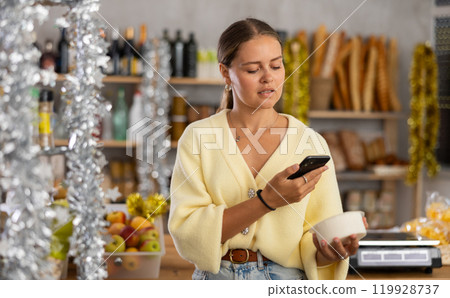 Young woman in store chooses cottage cheese, scan product label with phone 119928737