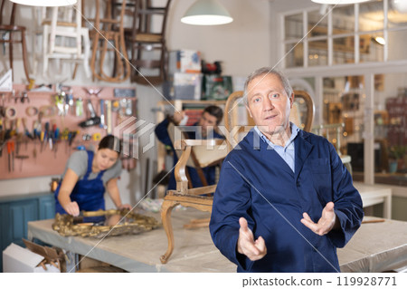 Master restoration worker dressed in overalls poses in working atmosphere of his workshop Master restoration worker dressed in overalls poses in working atmosphere of his workshop 119928771