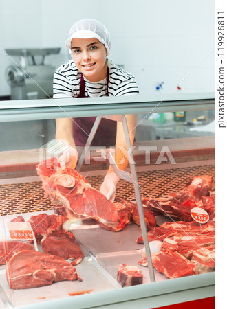 Young butcher shop saleswoman arranging raw beef in refrigerated display case Young butcher shop saleswoman arranging raw beef in refrigerated display case 119928811