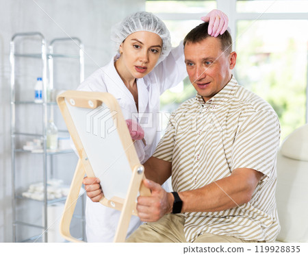 Portrait of man sitting on couch and looking at mirror during appointment with doctor at clinic Portrait of man sitting on couch and looking at mirror during appointment with doctor at clinic 119928835