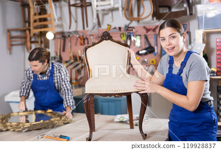 Professional craftswoman restorer in uniform renewing old-fashioned chair while working in repair shop 119928837