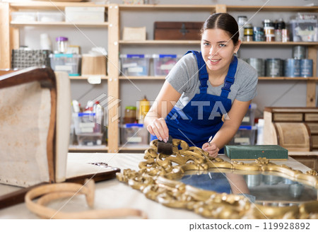 Young female furniture workshop worker repairing vintage mirror Young female furniture workshop worker repairing vintage mirror 119928892