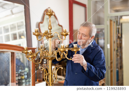 Older male furniture maker working on vintage chandelier in workshop Older male furniture maker working on vintage chandelier in workshop 119928893