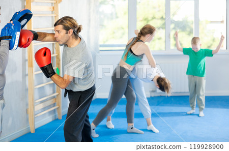 Man in boxing gloves practices punches with man in mitts in sport club during group training Man in boxing gloves practices punches with man in mitts in sport club during group training 119928900