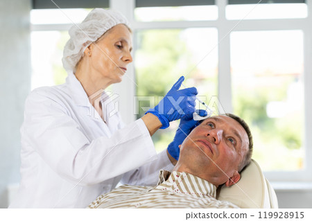 Man applying rejuvenating treatments by female doctor. Man applying rejuvenating treatments by female doctor. 119928915