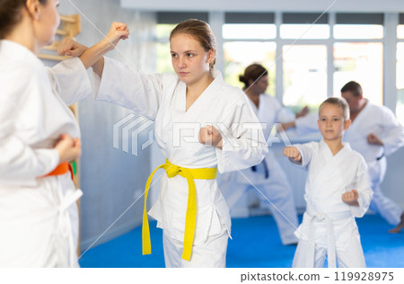 Teen girl is paired with mother to learn how to strike and rehearses blocking opponent 119928975