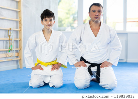 Karate trainer and student sitting on their knees on sports mats in gym 119929032