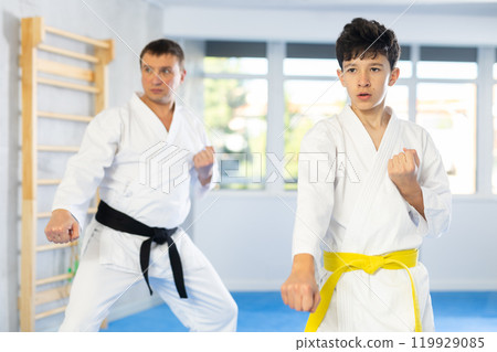 Teen boy and middle-aged man wearing kimono training karate techniques 119929085
