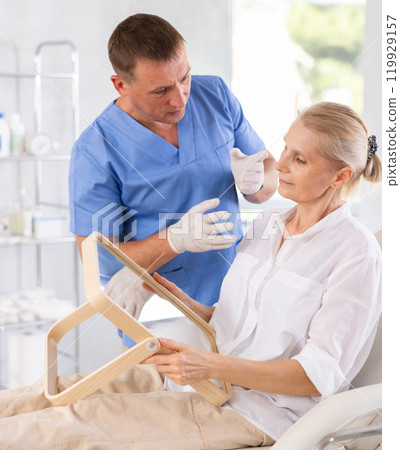 Senior woman looking at mirror while cosmetologist explaining facial procedure 119929157